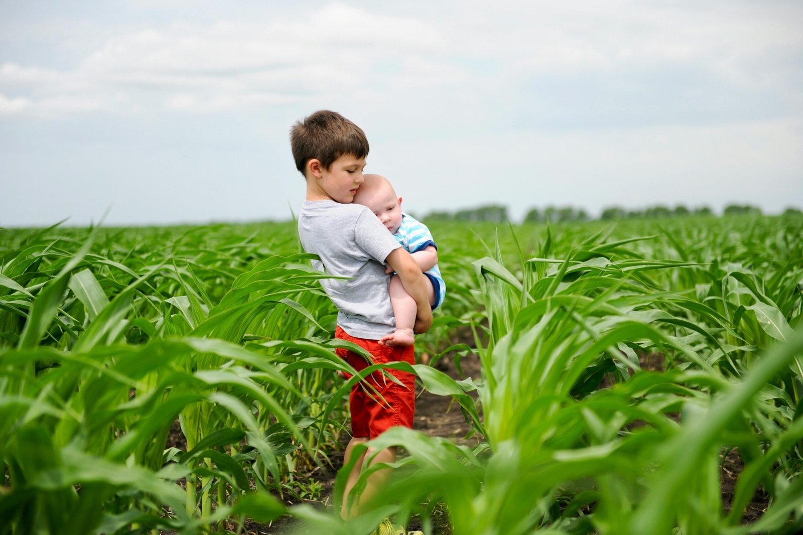 a young boy holding a baby in a field